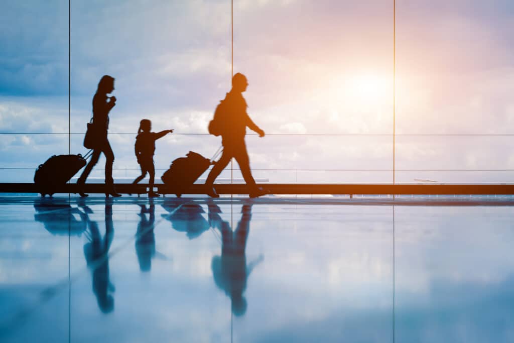 Voyage en famille : silhouettes dans un terminal d'aéroport Famille voyageant avec valises en silhouette dans un terminal d'aéroport lumineux, reflets sur le sol.