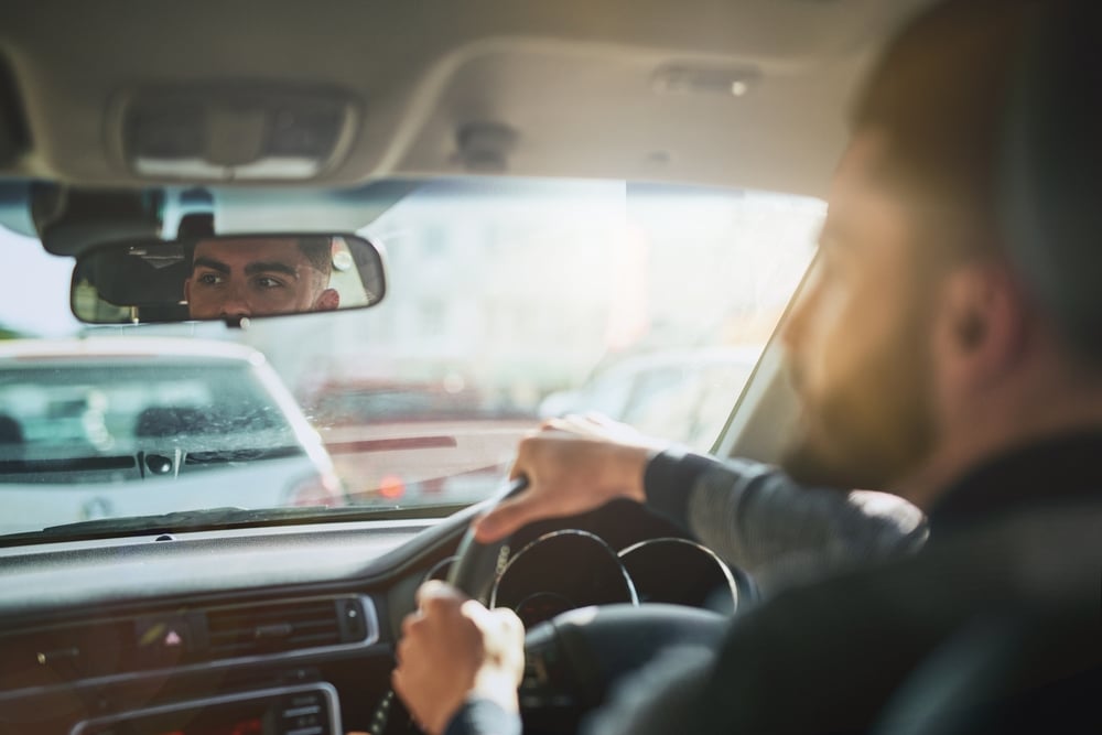 Homme au volant et reflet dans le rétroviseur intérieur Homme conduisant avec attention, regard reflété dans le rétroviseur intérieur et route visible à travers le pare-brise.