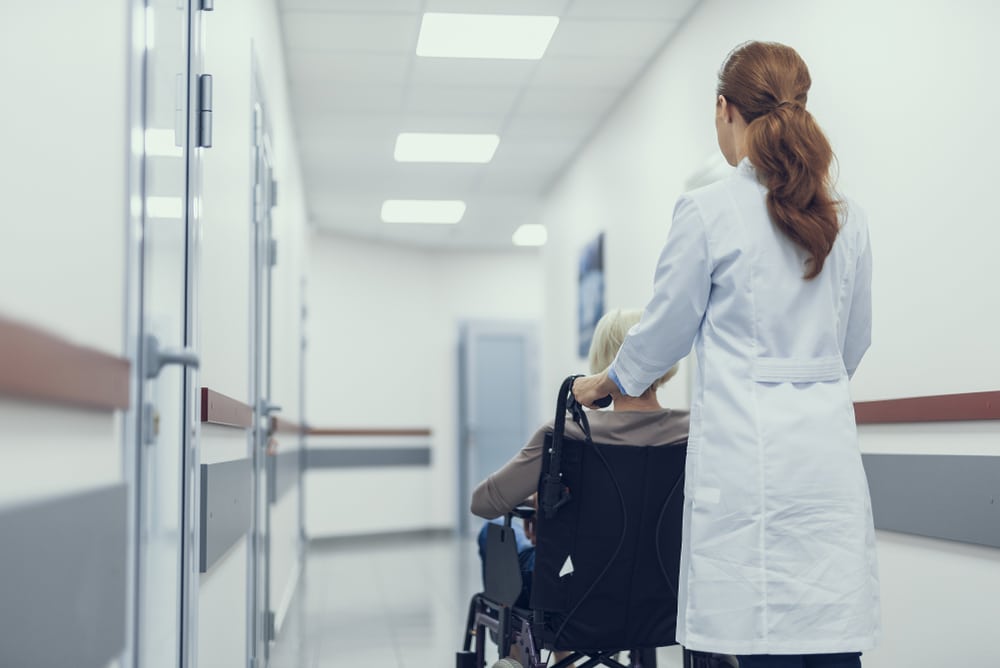 Woman,In,Medical,Uniform,Is,Pushing,Wheelchair,With,Sitting,Patient.