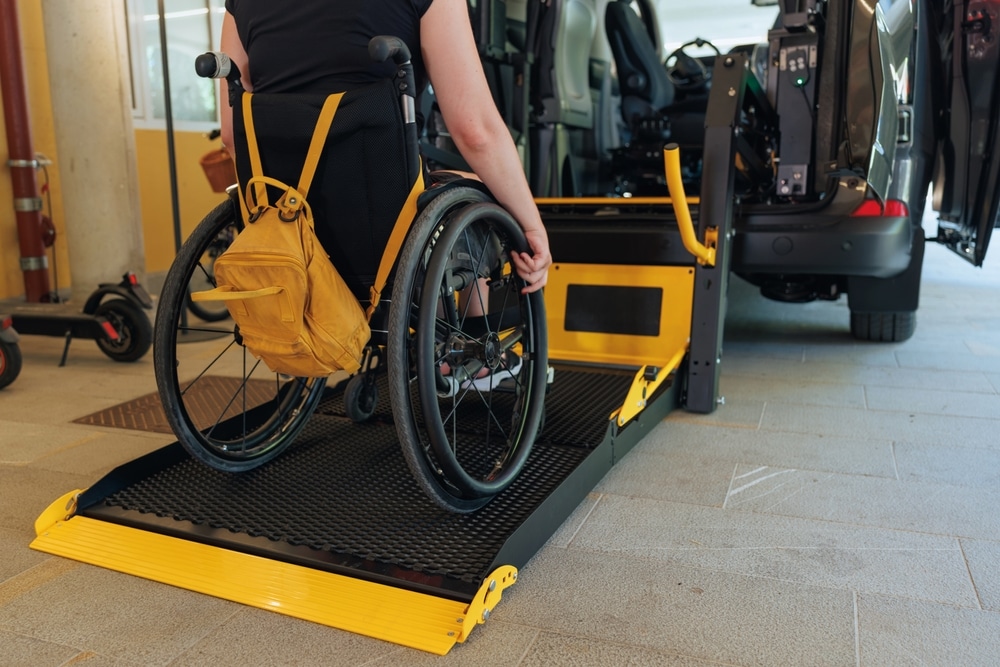 Femme en fauteuil roulant utilisant une plateforme élévatrice jaune pour monter dans un véhicule adapté.