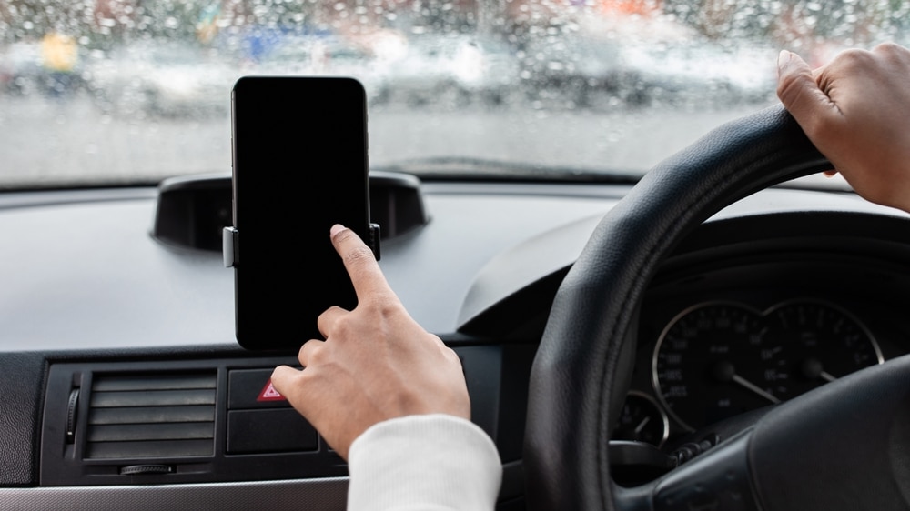 Smartphone en voiture : Utilisation et Sécurité Routière Main de conducteur utilisant un smartphone fixé au tableau de bord d'une voiture par temps de pluie.